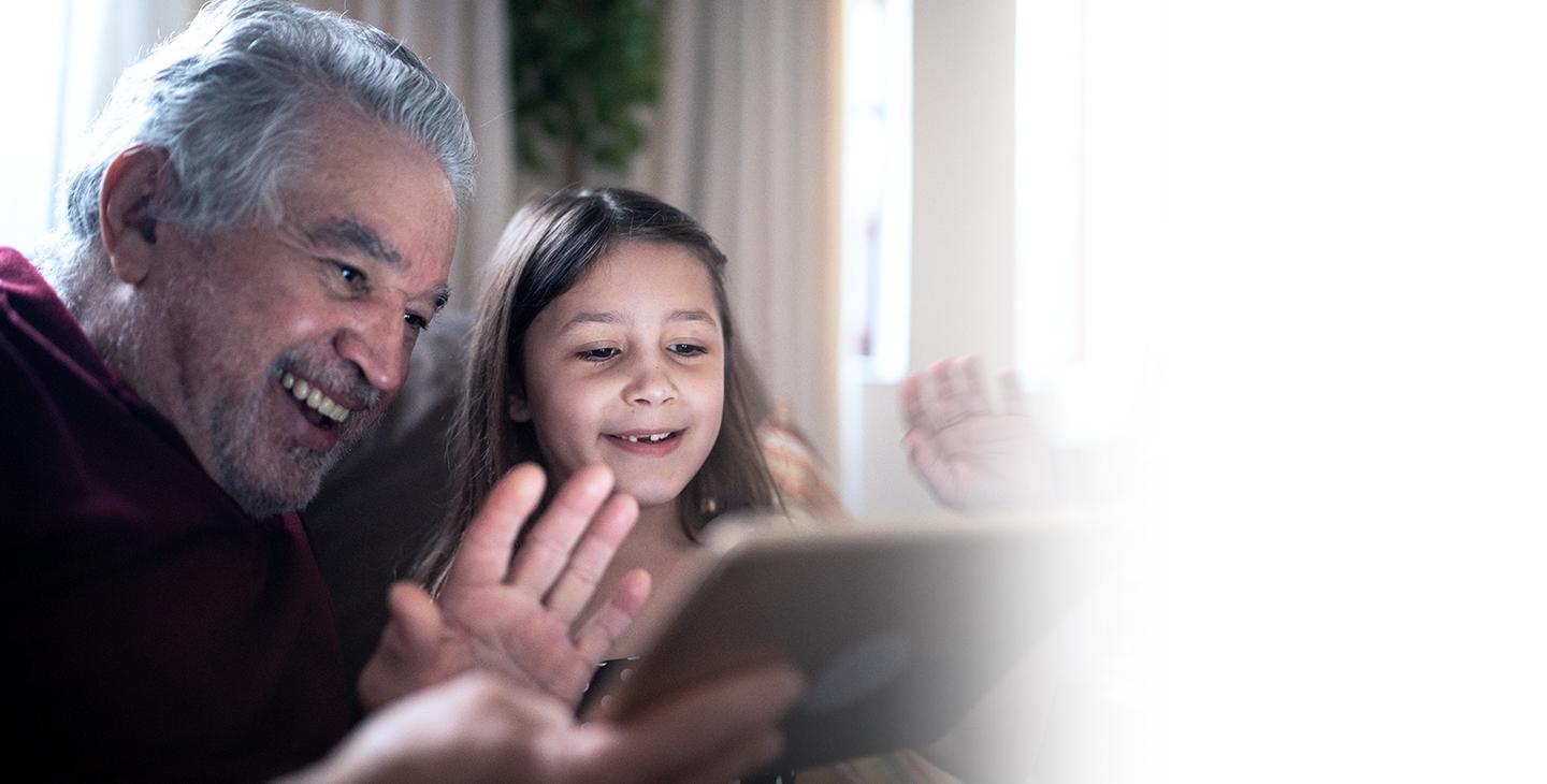 Child sitting with her grandfather staying connected to the internet on their tablet with help from the FCC's Affordable Connectivity Program.